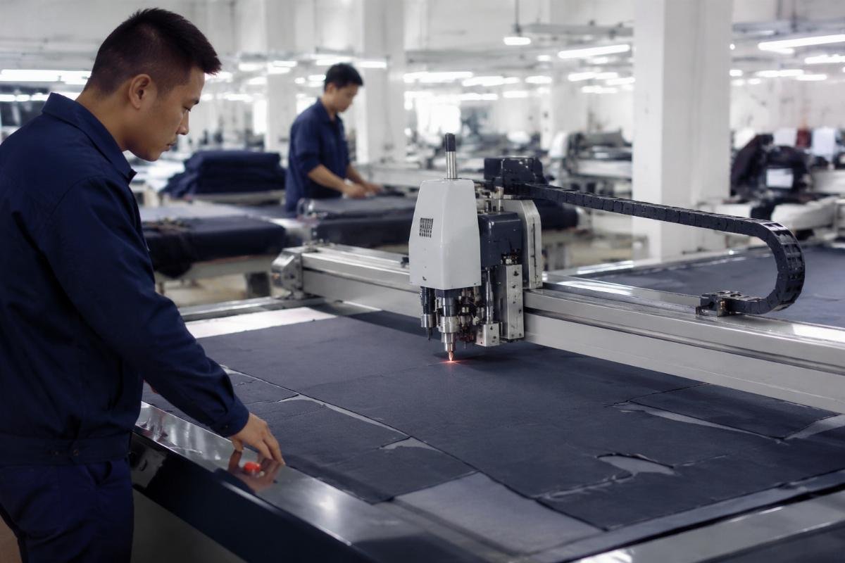 Garment factory CNC oscillating knife machine in operation Workers operating a CNC oscillating knife machine in a garment factory